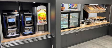 A self-service beverage station with two coffee machines and a refrigerated display case.