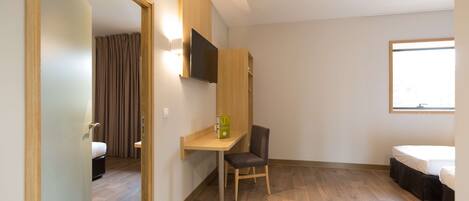 Une chambre d’hôtel moderne, équipée d’un bureau en bois, d’une chaise, d’un lit et d’un téléviseur fixé au mur.