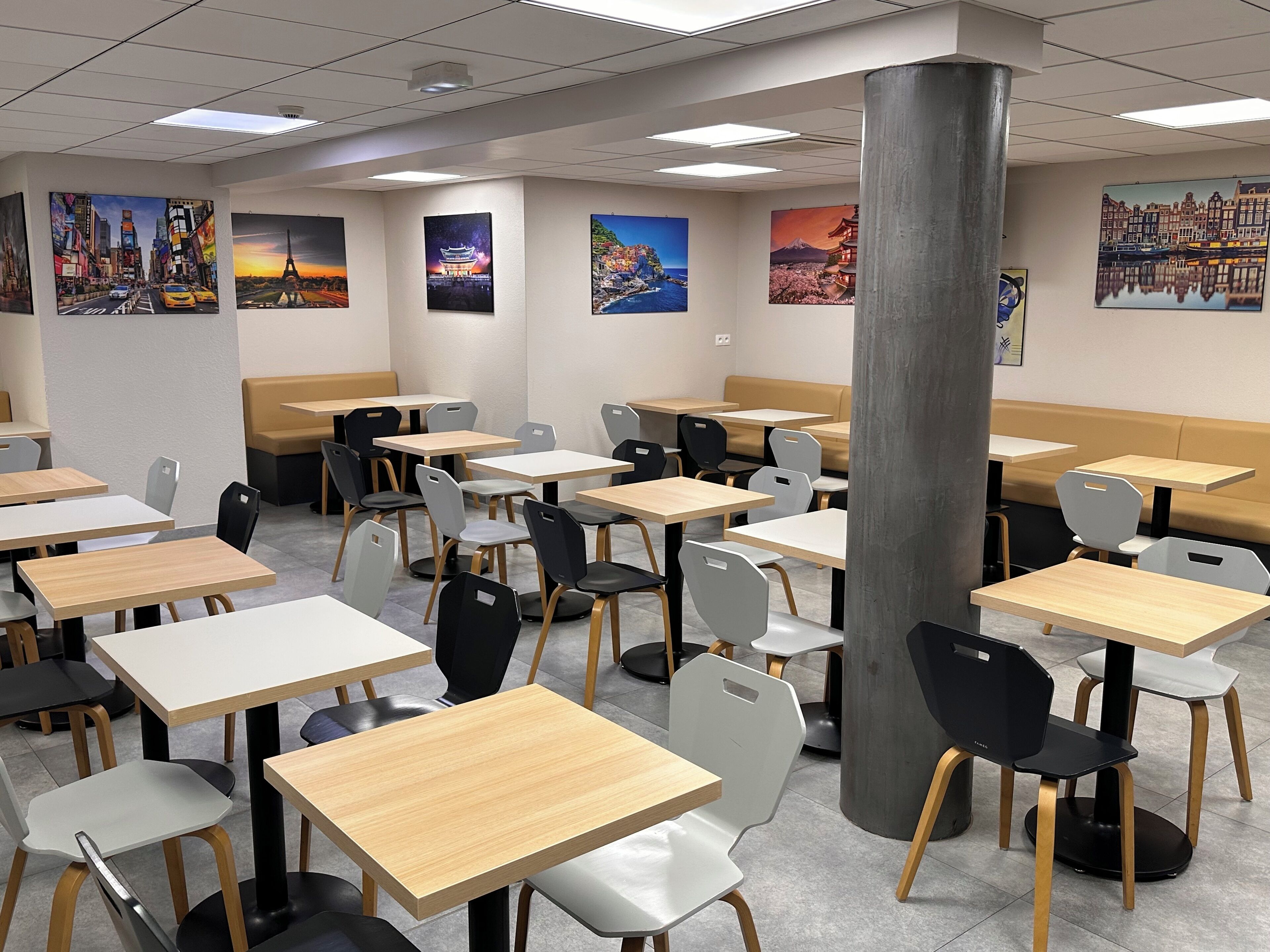 A modern dining area with multiple tables and chairs, a large pillar, and cityscape artwork on the walls.