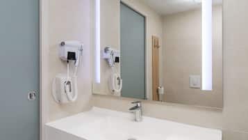 Un baño con un lavamanos blanco, dos secadores de pelo sujetos a la pared, un espejo y una puerta.