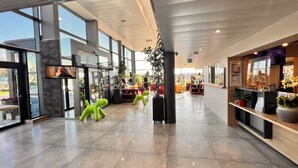 Un hall d’entrée spacieux, doté de grandes fenêtres, d’un comptoir de réception et d’un espace détente avec des fauteuils d’un vert vif.