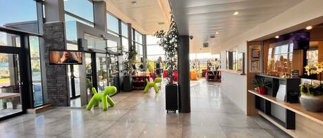 Un vestíbulo espacioso con grandes ventanales, un mostrador de recepción y una zona de estar con sillas de color verde brillante.