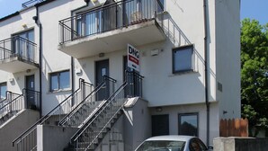 A multi-story building with a 'For Rent' sign, a car parked in front, and a staircase leading to the entrance.