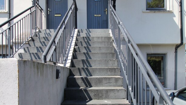 A set of concrete stairs with metal railings leading to a building with two doors.