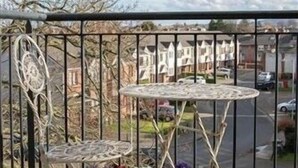 A balcony with two white tables and chairs, surrounded by a metal fence.