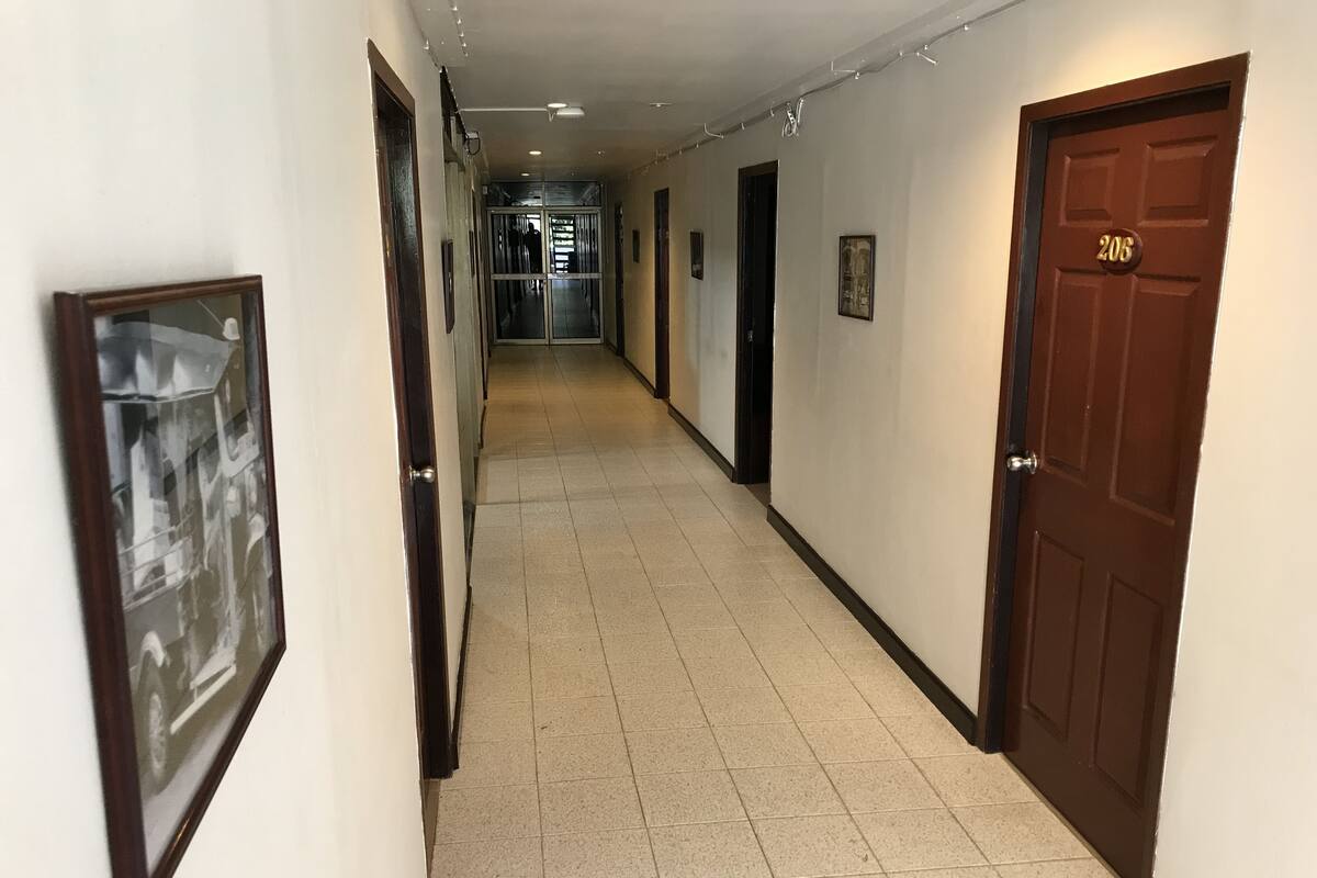 Un pasillo con suelo de baldosas, cuadros en las paredes y una puerta con el número 206.