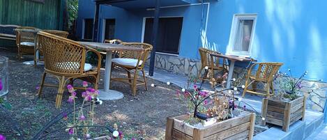 An outdoor seating area with wicker chairs and a table, surrounded by potted plants and flowers.