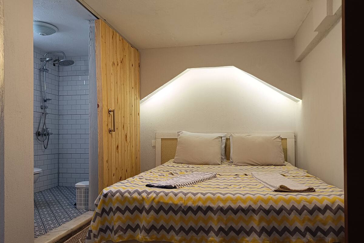 Ein kleines, gemütliches Schlafzimmer mit einem Bett, einem Holzschrank und einer Duschkabine.