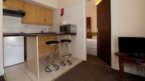 A compact kitchen with wooden cabinets, a microwave, a refrigerator, and two bar stools. A television is placed on a wooden table to the right. - Gardiner Street Self Catering (Dublin)
