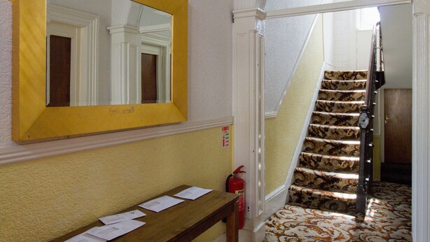 A hallway with a wooden bench, a mirror, and a staircase. - Gardiner Street Self Catering (Dublin)