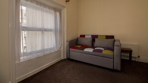 A room with a window, a radiator, and a sofa with a colorful cushion. - Gardiner Street Self Catering (Dublin)