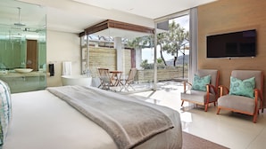 Une chambre moderne dotée d’un grand lit, d’une douche à parois de verre, d’un coin salon avec des fauteuils et d’un téléviseur fixé au mur.