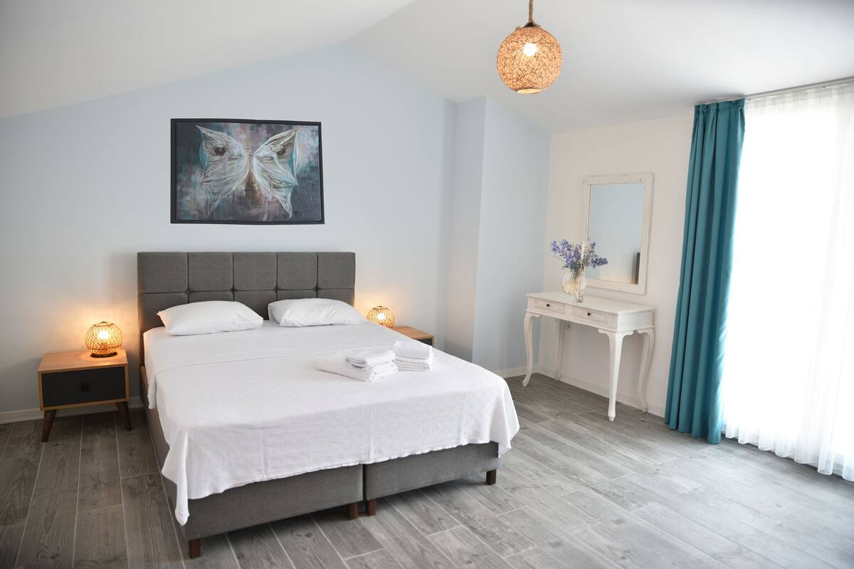 A bedroom with a bed, bedside lamps, a dresser, a mirror, and a painting on the wall.