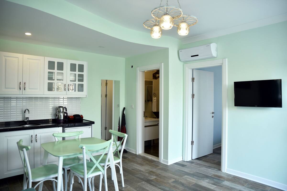 A modern kitchen with white cabinets, a black countertop, and a dining area with green chairs.