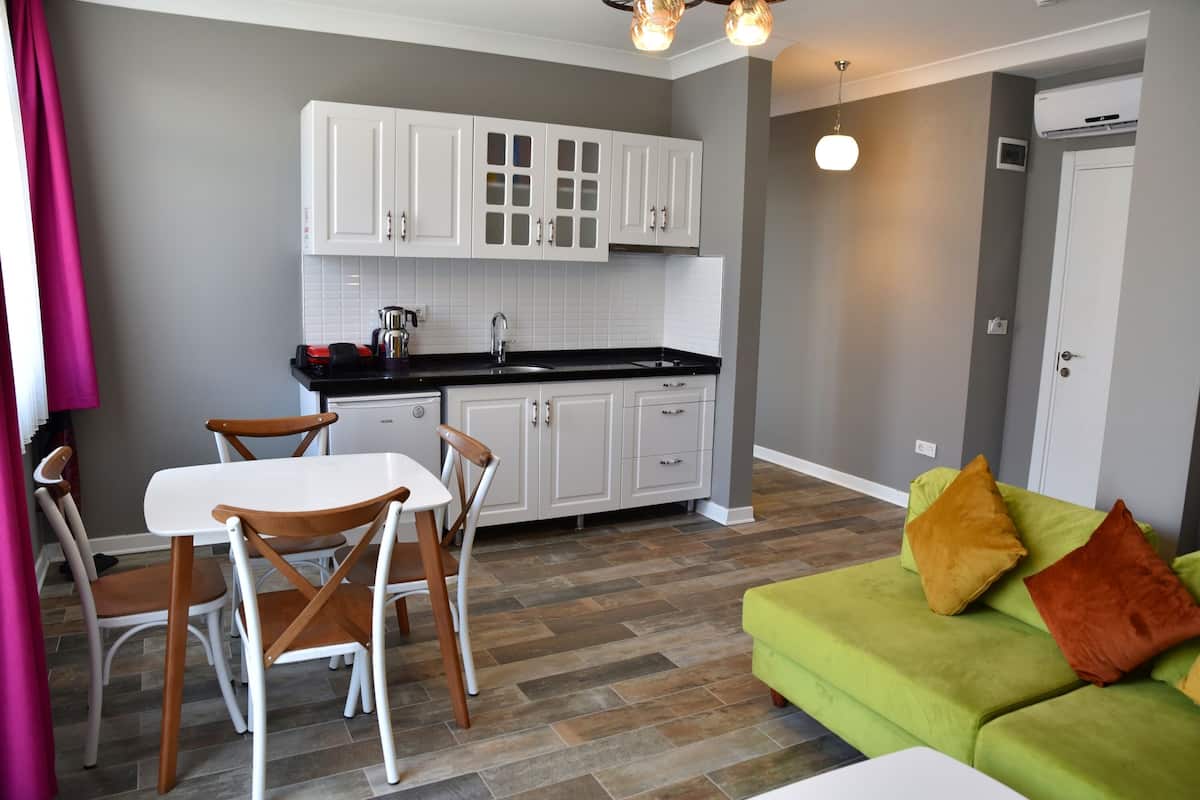 A modern kitchen with white cabinets, a dining area with a white table and wooden chairs, and a green sofa with cushions.