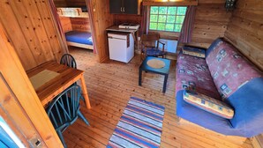 A cozy cabin interior with a wooden ceiling, a dining table with chairs, a sofa, a small kitchenette, and a window with curtains. - Tana Familiecamping (Tana)