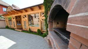 Un edificio de madera con un horno de ladrillo, un porche cubierto y una entrada con ventanas.