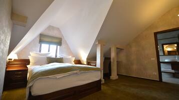 A bedroom with a sloped ceiling, a bed, bedside tables, and a bathroom visible through an open door.