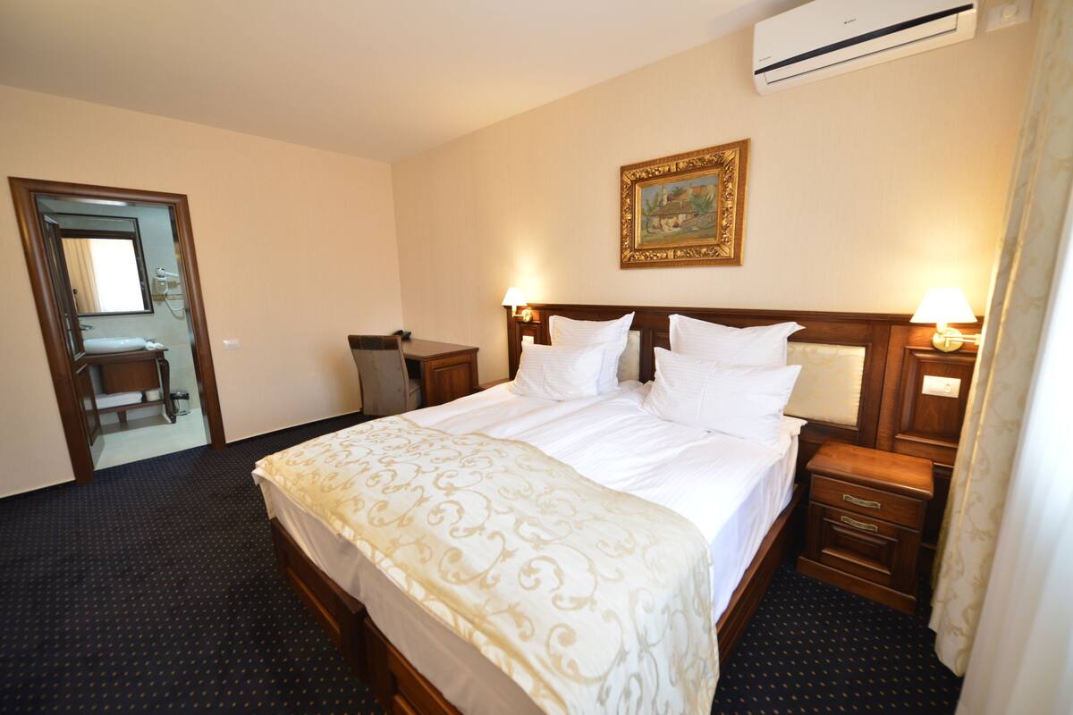 A hotel room with a large bed, bedside tables, a mirror, and an air conditioning unit.