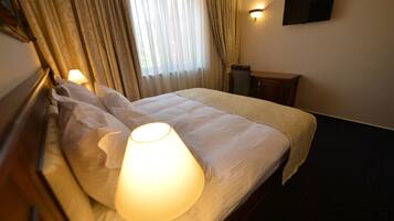 A hotel room with a bed, a bedside lamp, a TV mounted on the wall, and a small table.