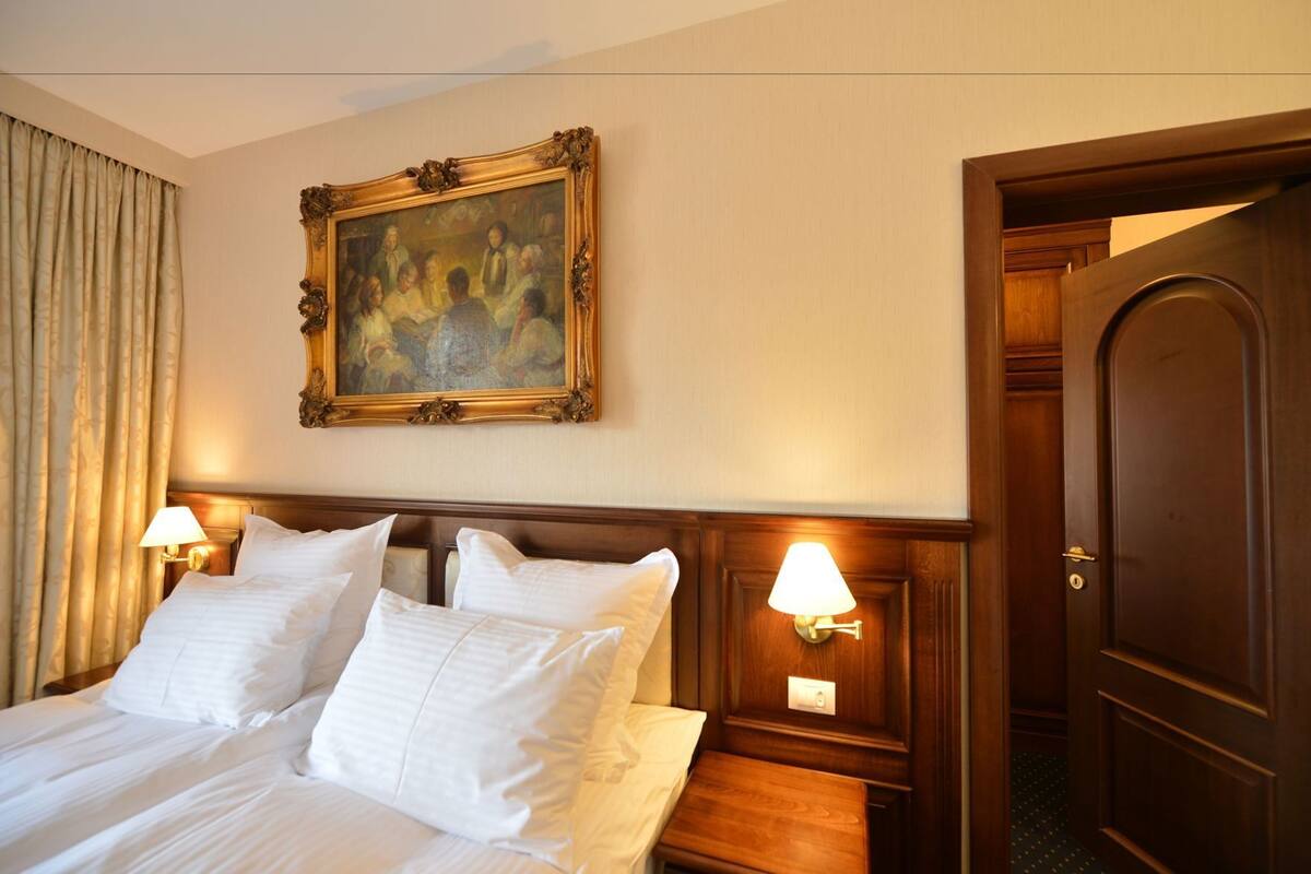 A hotel room with a large bed, two bedside lamps, a painting above the bed, and a wooden door.