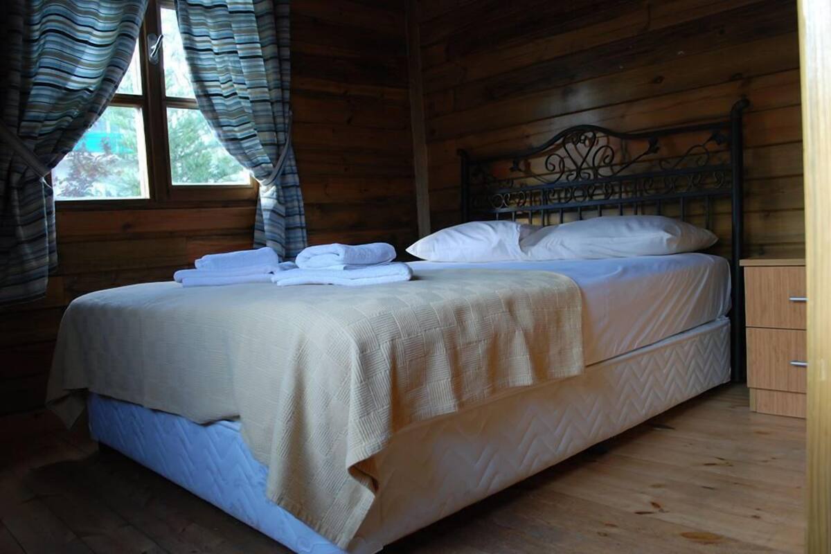 A wooden cabin bedroom with a bed, curtains, and a window.