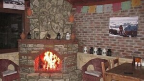 A stone fireplace with a fire, surrounded by stone walls and a brick section. There are chairs and a table in front of the fireplace. - Agva Himalaya Motel (Sile)