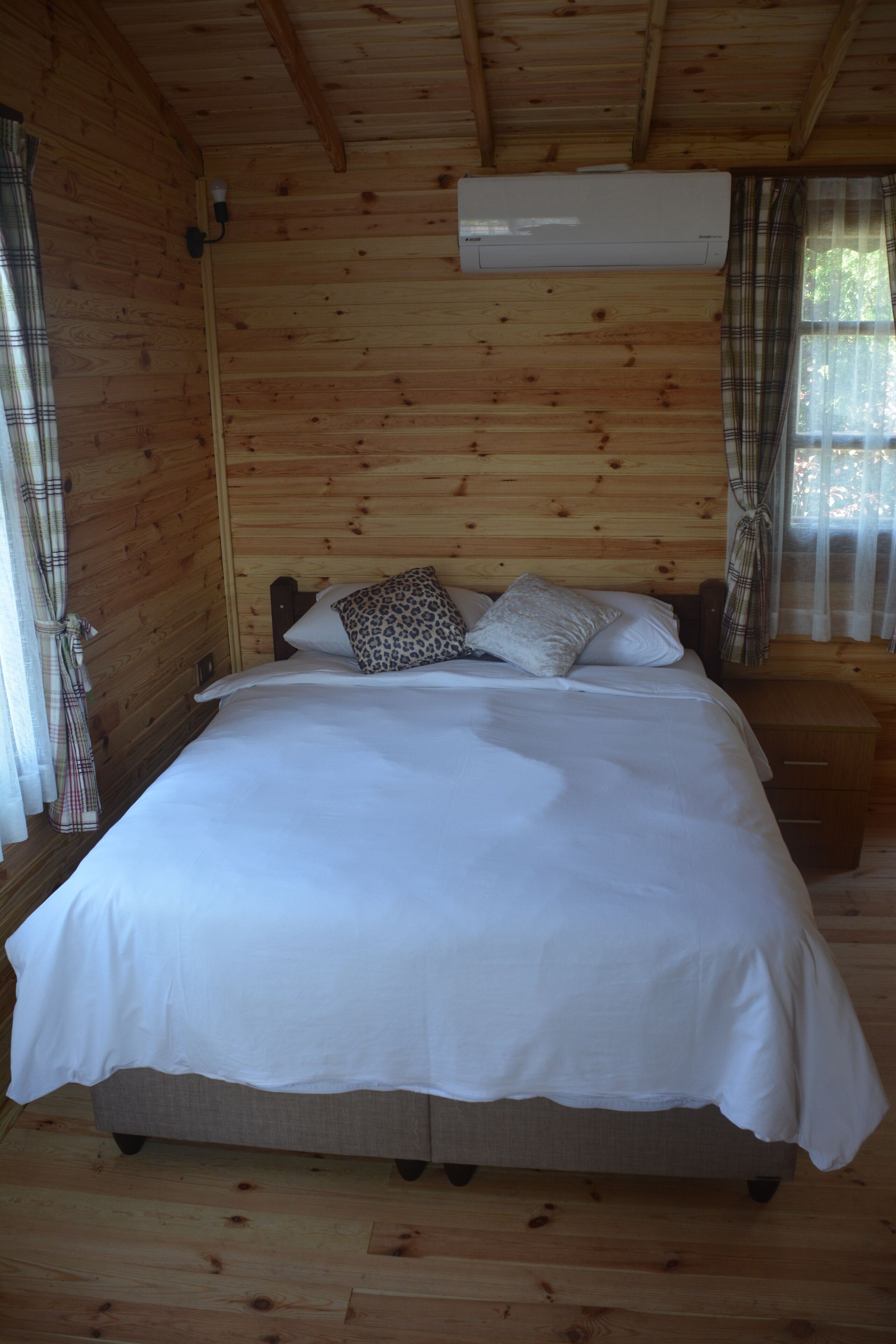 Ein Zimmer mit Holzwänden, einem Bett, einem Nachttisch und einer Klimaanlage.