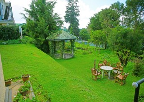 A lush garden with a gazebo, a small table, and wooden chairs.