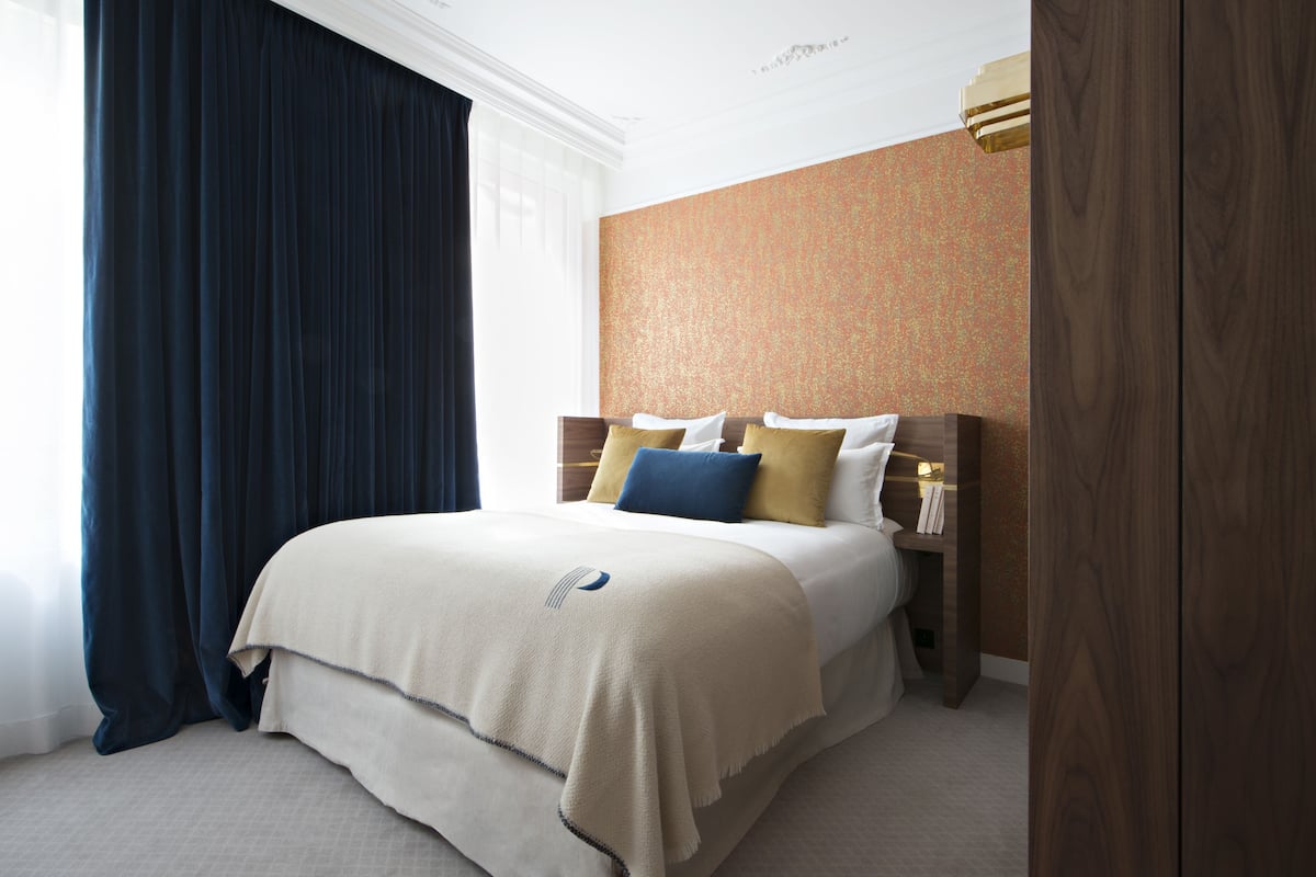 A neatly made bed with a beige blanket, a wooden headboard, and a nightstand with a lamp.
