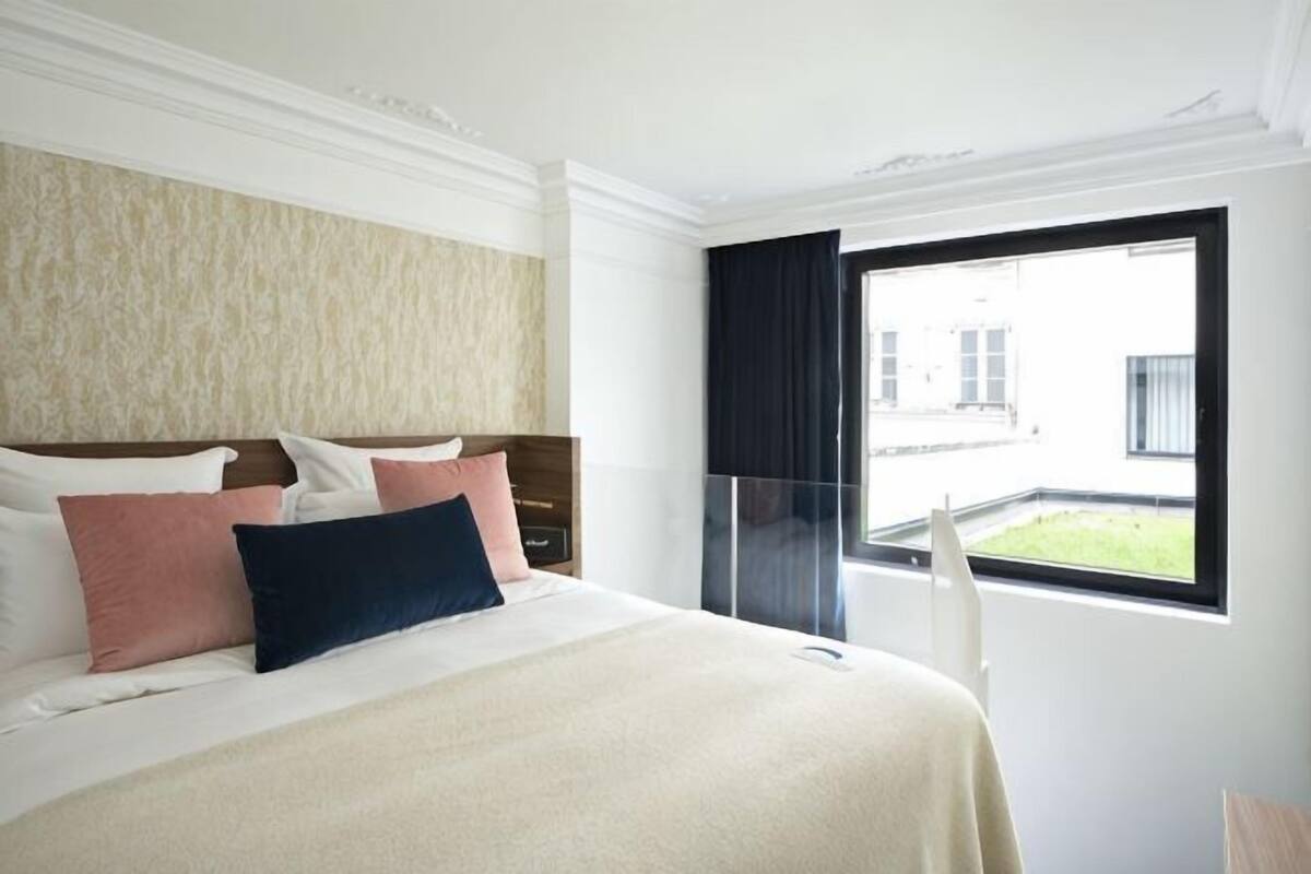 A hotel room with a bed, a window, and a view of the outside.