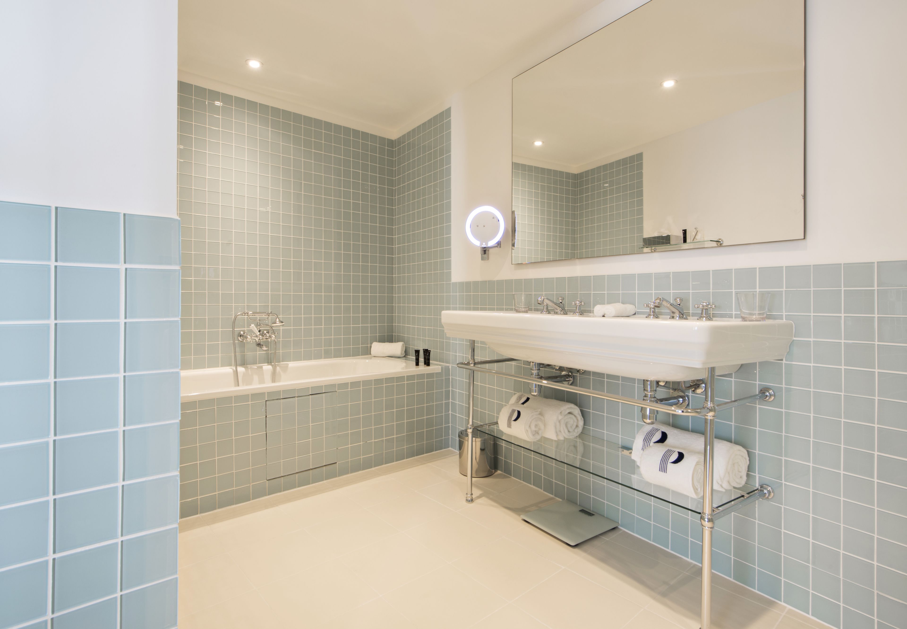A modern bathroom with a white sink, a large mirror, and a built-in shelf for towels.