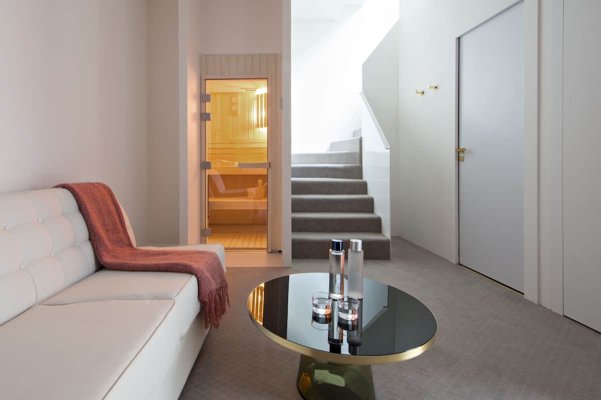 A modern living room with a white sofa, a glass coffee table, and a staircase leading to a wooden interior.