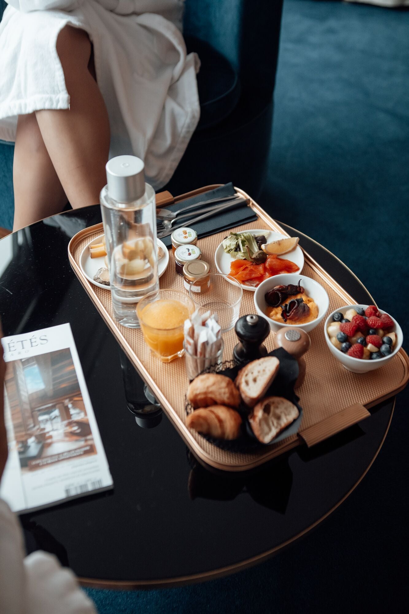 A tray with breakfast items including croissants, fruit, and a bottle of water on a table.