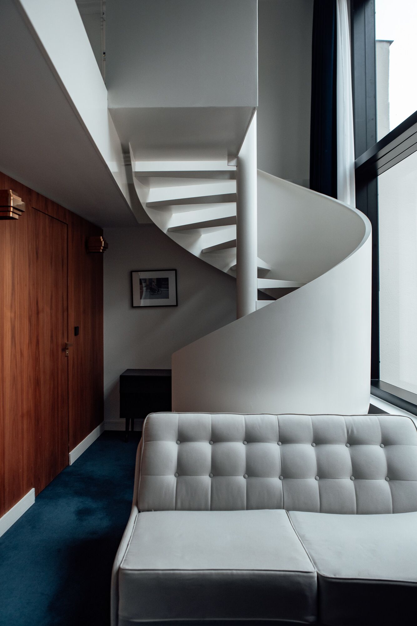 A modern interior with a spiral staircase, a wooden door, and a grey upholstered sofa.