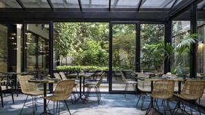 An indoor dining area with glass walls, wicker chairs, and tables. - Hotel Parister & Spa (Paris)