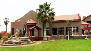 A two-story house with a red roof, a small patio with a fountain, and a well-maintained lawn. - Amjicaja Guesthouse (Walvis Bay)