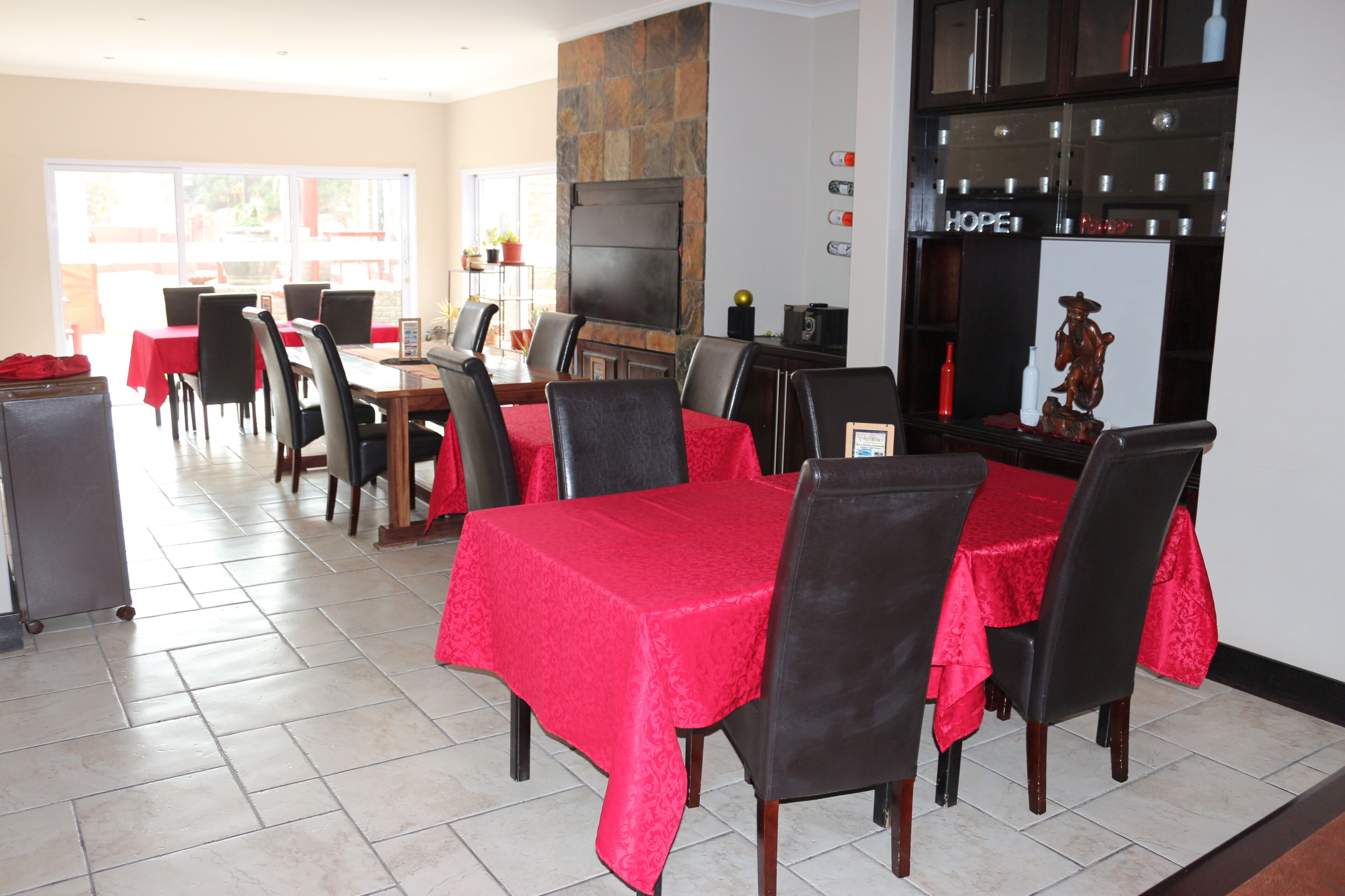 A dining area with red tablecloths, black chairs, and a stone fireplace.