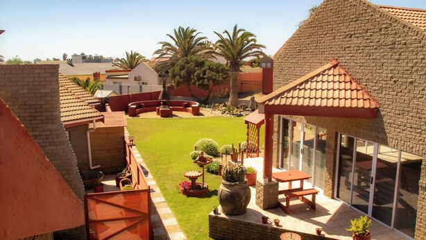A patio area with a brick wall, a wooden deck, and a glass door leading to an outdoor space. - Amjicaja Guesthouse (Walvis Bay)