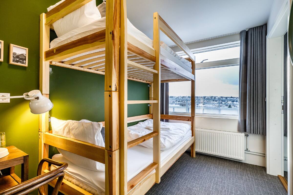 A bunk bed room with a view of a cityscape through a window.