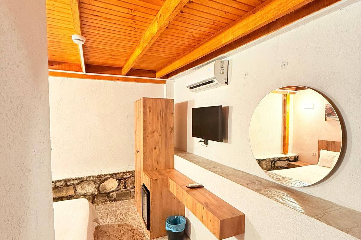 A bathroom with a wooden ceiling, a stone wall, a mirror, a television, and a towel hanging on the wall.