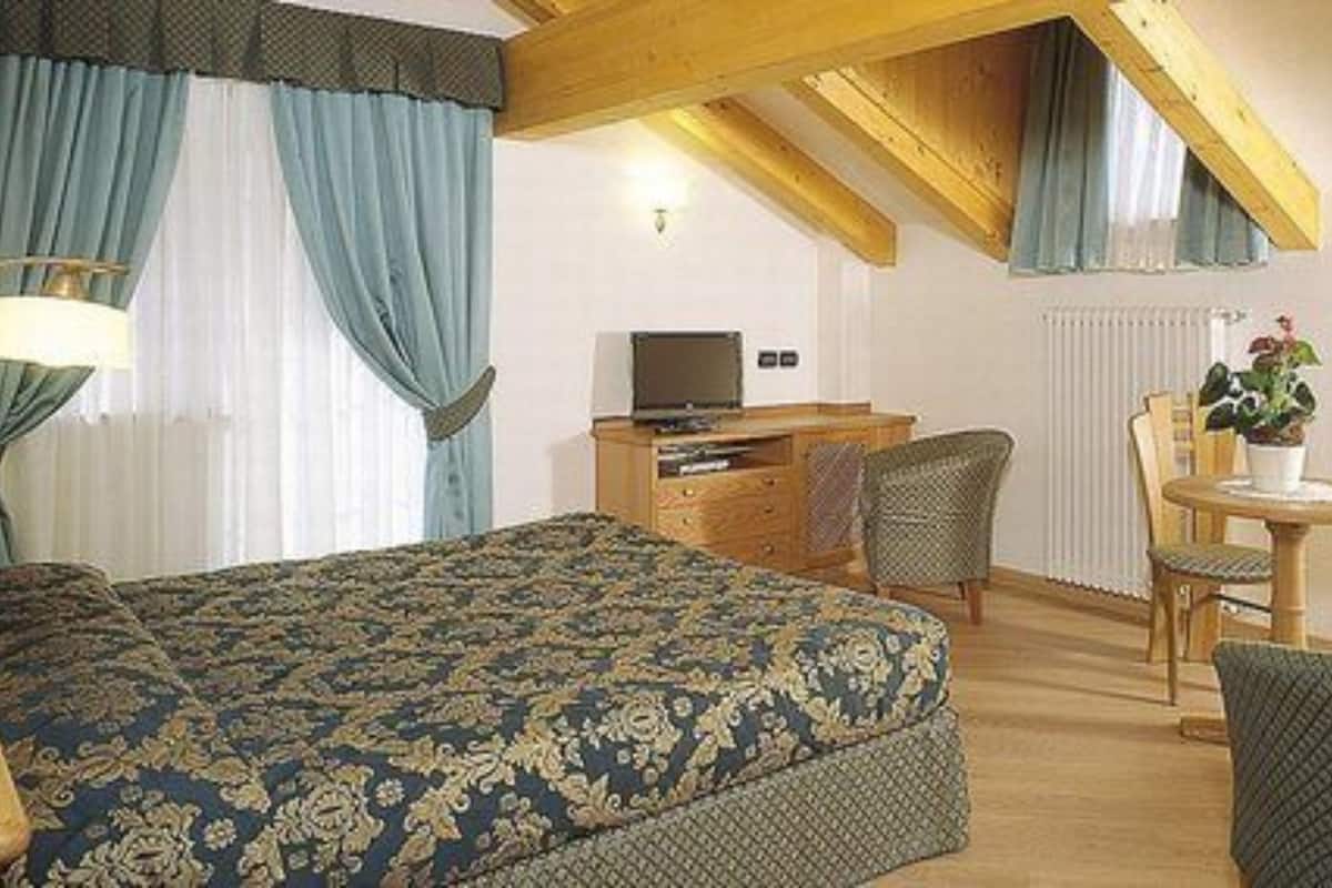 A bedroom with a large bed, a desk, a chair, and a small table with a plant.