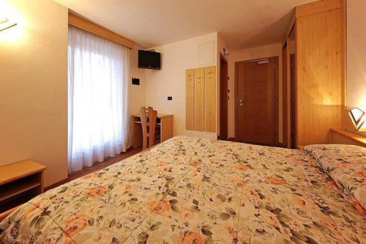 A hotel room with a bed, a desk, a chair, a TV mounted on the wall, and a wardrobe.