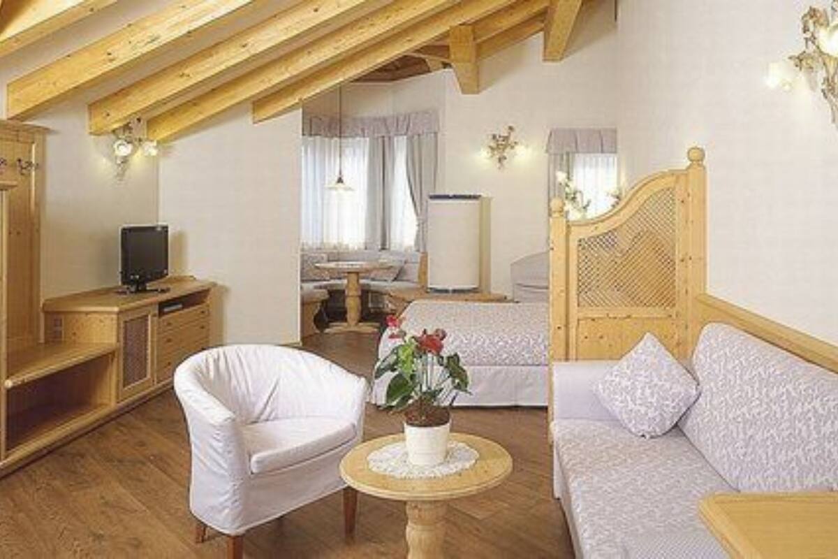 A cozy room with a wooden ceiling, a white sofa, a white armchair, a small round table with a plant, and a bed with a wooden headboard.