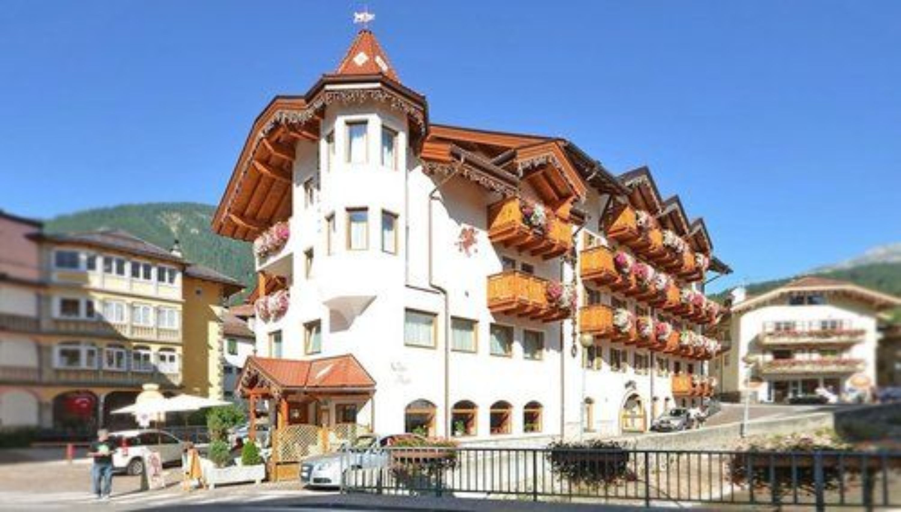 Un edificio de varios pisos con balcones decorados con flores, una torre destacada con una estrella en la cima, y un cielo azul despejado al fondo.