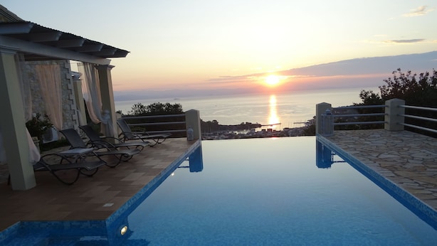 An infinity pool with a view of the sunset over the sea, lounge chairs, and a pergola. - Artist's Villa Red Rose (Paxos)