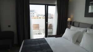 Habitación de hotel con una cama, una silla, una mesa y vistas a la ciudad a través de una puerta corrediza de vidrio.