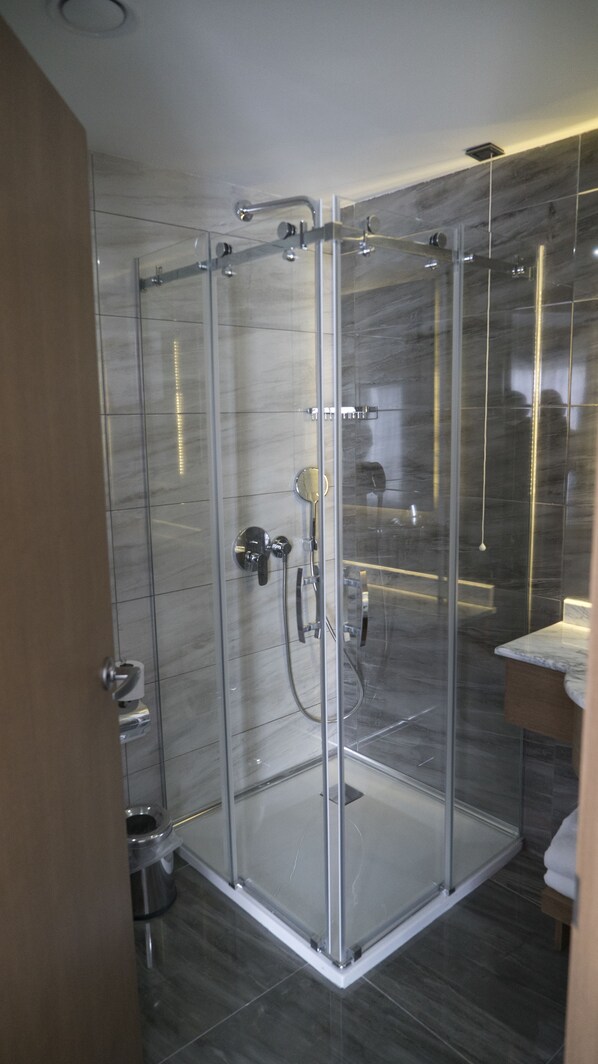 A modern bathroom with a glass-enclosed shower, marble tiles, and a wooden vanity.