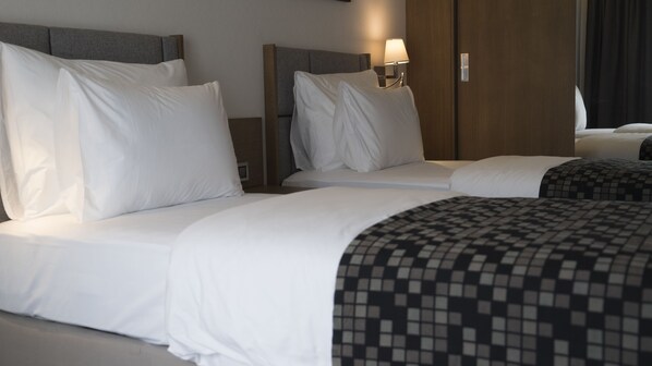 Une chambre d’hôtel avec deux lits, chacun doté de draps blancs et d’une tête de lit. On y trouve une table de chevet avec une lampe, ainsi qu’un mur revêtu de panneaux en bois.