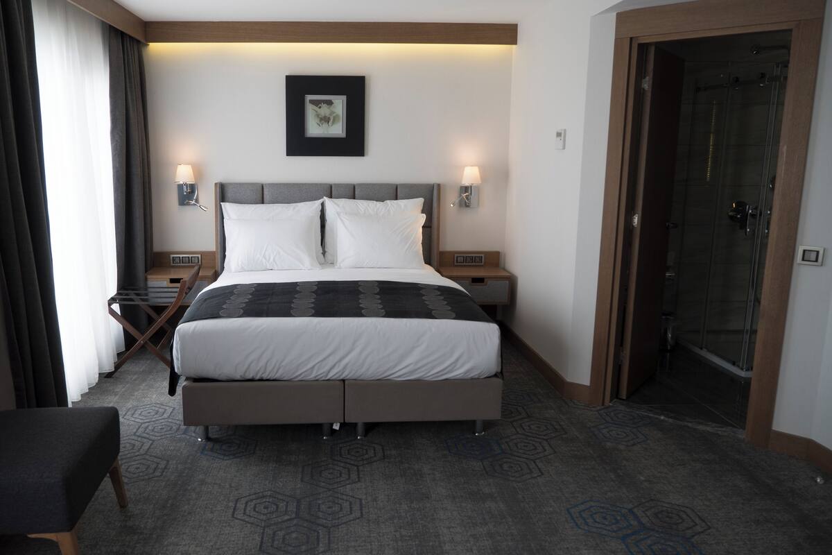 A hotel room with a large bed, two bedside tables, a chair, a shower, and a door.